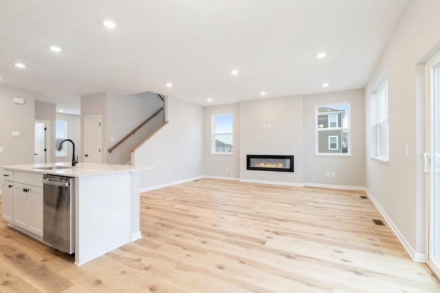 kitchen with a kitchen island with sink, sink, stainless steel dishwasher, and light hardwood / wood-style flooring