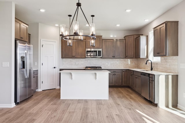 kitchen with tasteful backsplash, stainless steel appliances, pendant lighting, light hardwood / wood-style floors, and a kitchen island