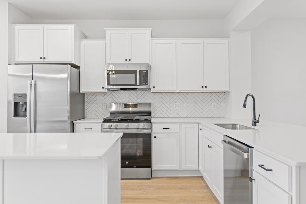 kitchen with decorative backsplash, appliances with stainless steel finishes, sink, light hardwood / wood-style flooring, and white cabinetry