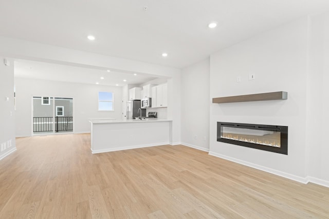 unfurnished living room with light hardwood / wood-style flooring and sink