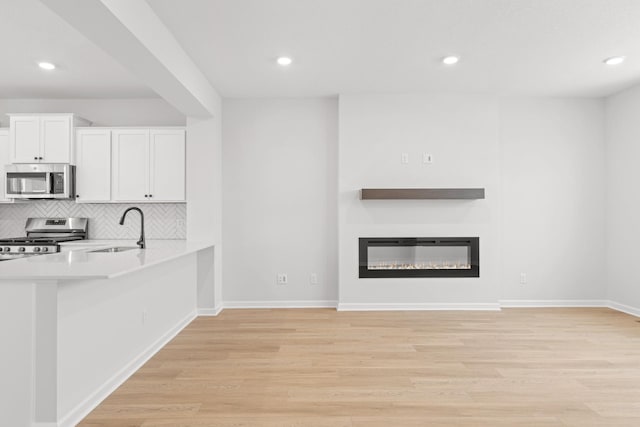 kitchen with white cabinets, sink, appliances with stainless steel finishes, and light hardwood / wood-style flooring