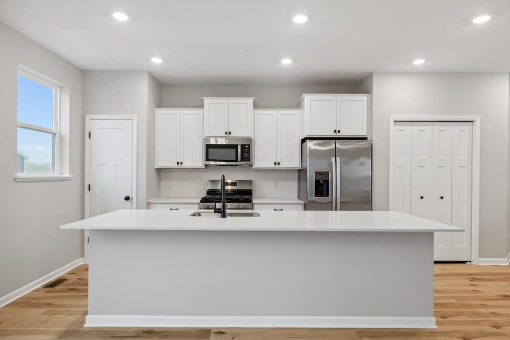 kitchen with white cabinetry, sink, stainless steel appliances, an island with sink, and light wood-type flooring