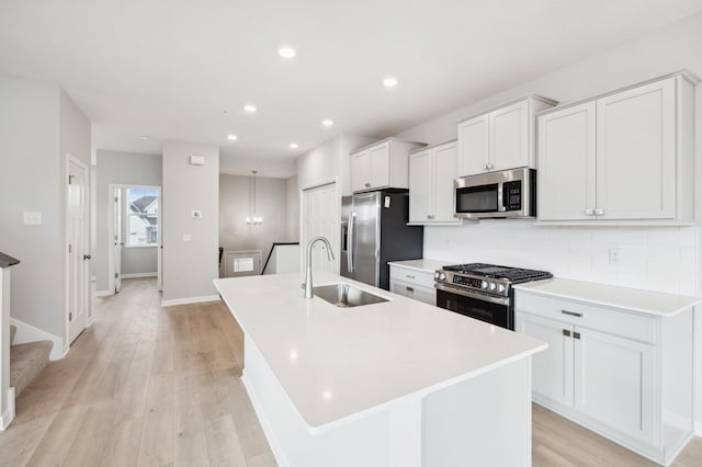 kitchen with sink, stainless steel appliances, white cabinetry, and an island with sink