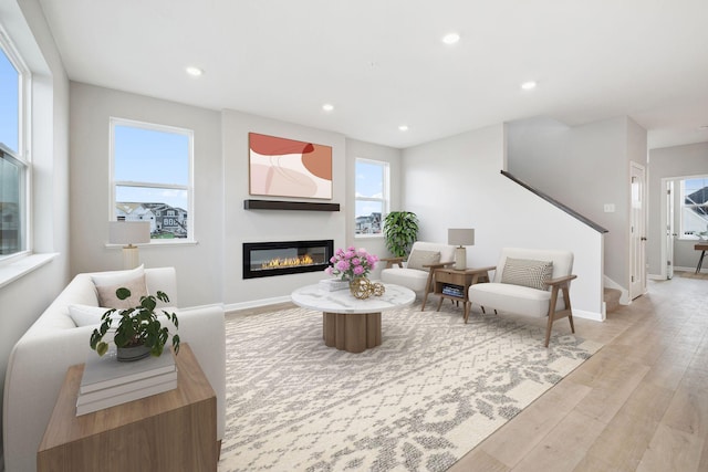 living area featuring baseboards, light wood finished floors, a glass covered fireplace, and recessed lighting