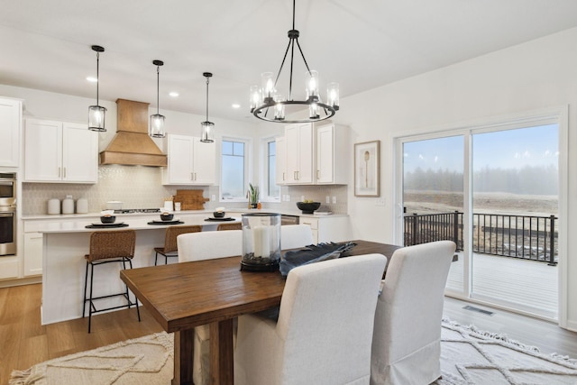 dining room featuring an inviting chandelier, light hardwood / wood-style flooring, a wealth of natural light, and a water view