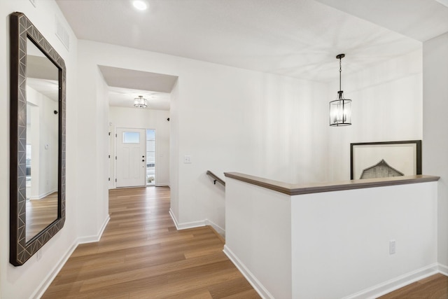 hall featuring baseboards, an upstairs landing, wood finished floors, and a chandelier