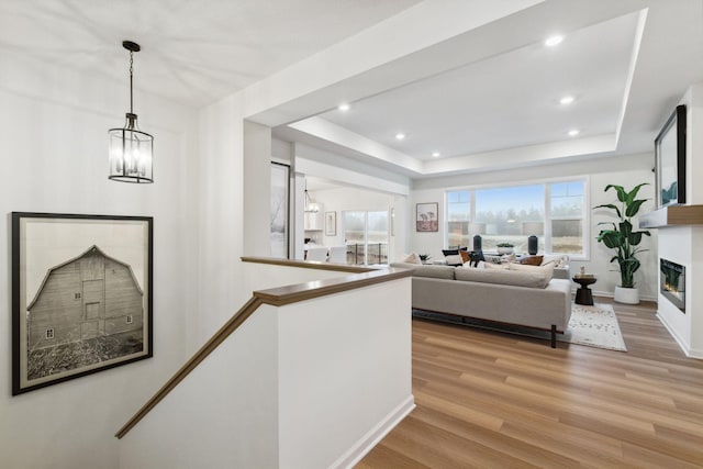 living area with an inviting chandelier, recessed lighting, light wood-style floors, a glass covered fireplace, and a raised ceiling