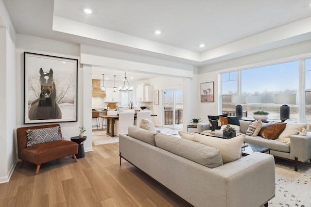 living area featuring recessed lighting, a raised ceiling, light wood-style floors, and a chandelier