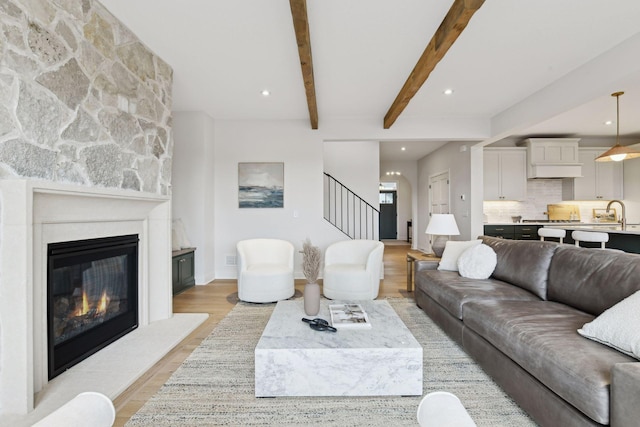 living room with beam ceiling, a stone fireplace, and light hardwood / wood-style flooring