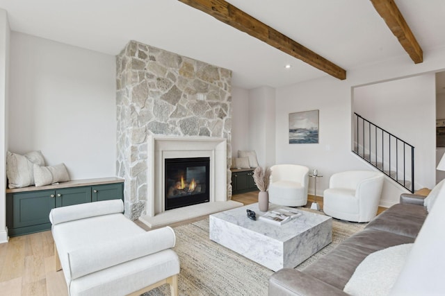 living room featuring a stone fireplace, light hardwood / wood-style flooring, and beamed ceiling