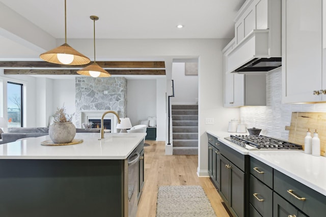 kitchen with stainless steel gas cooktop, decorative light fixtures, a center island with sink, beamed ceiling, and white cabinetry