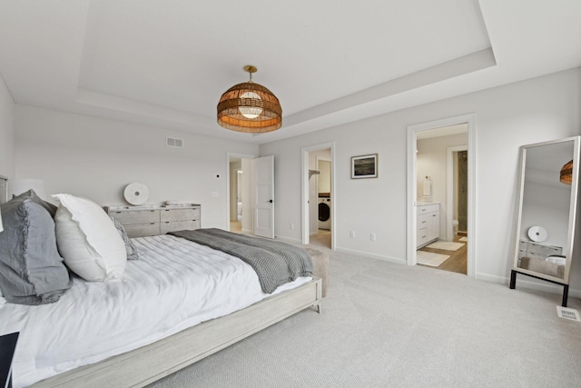 bedroom featuring a raised ceiling, ensuite bath, washer / clothes dryer, and light carpet