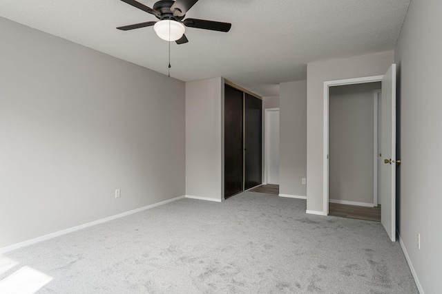 unfurnished bedroom with ceiling fan, a closet, light carpet, and a textured ceiling