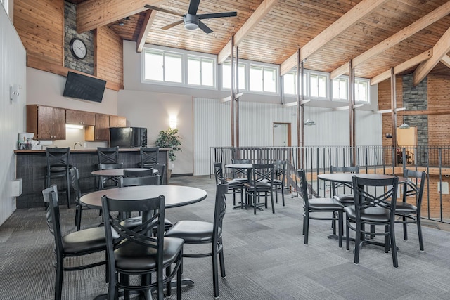 dining area with beamed ceiling, ceiling fan, carpet floors, and a high ceiling