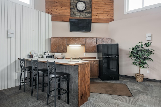 kitchen with a kitchen breakfast bar, kitchen peninsula, black refrigerator, and a towering ceiling