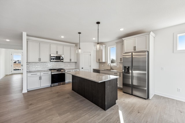 kitchen with sink, light stone counters, decorative light fixtures, a center island, and appliances with stainless steel finishes