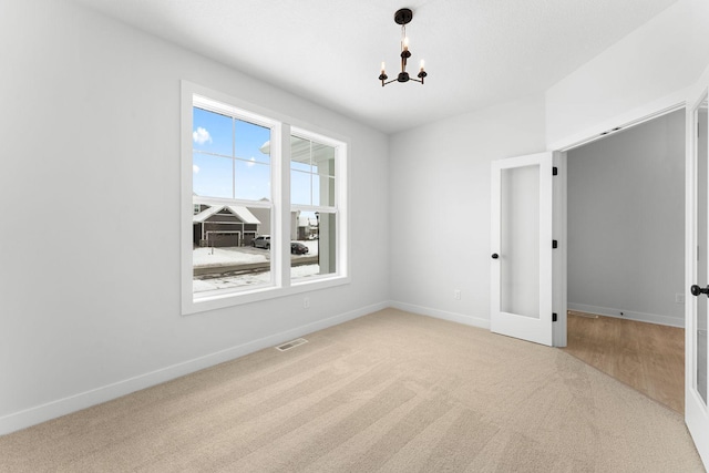 empty room featuring light carpet, an inviting chandelier, and french doors