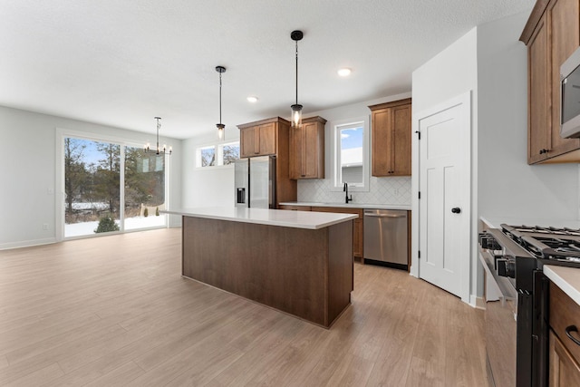 kitchen with appliances with stainless steel finishes, hanging light fixtures, a center island, light hardwood / wood-style floors, and decorative backsplash