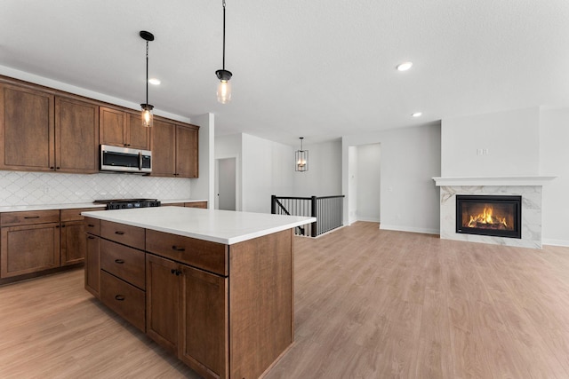 kitchen featuring tasteful backsplash, light hardwood / wood-style flooring, a kitchen island, pendant lighting, and a premium fireplace