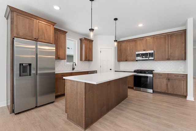 kitchen featuring sink, decorative light fixtures, light hardwood / wood-style flooring, appliances with stainless steel finishes, and a kitchen island