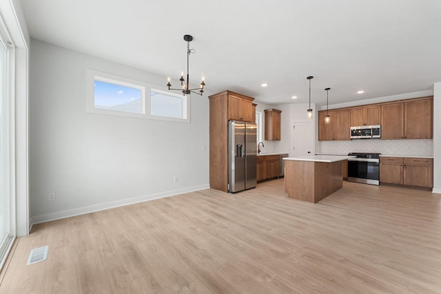 kitchen with decorative light fixtures, stainless steel appliances, light hardwood / wood-style floors, and a kitchen island