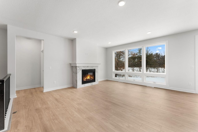 unfurnished living room featuring light hardwood / wood-style floors, a premium fireplace, and a textured ceiling