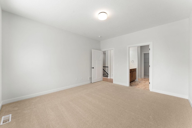 unfurnished bedroom featuring ensuite bath and light colored carpet