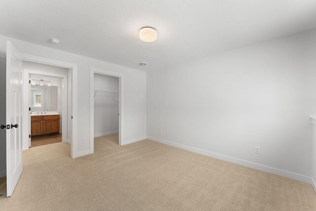 unfurnished bedroom featuring sink, a textured ceiling, light carpet, a walk in closet, and a closet