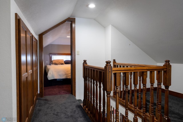 hall with dark carpet, vaulted ceiling, and a textured ceiling