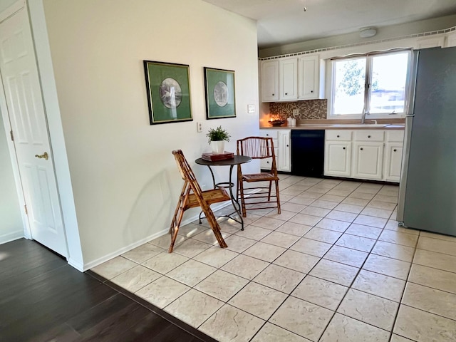 kitchen featuring backsplash, light tile patterned floors, black dishwasher, white cabinetry, and stainless steel refrigerator