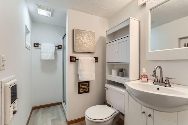 bathroom with vanity, toilet, a textured ceiling, a shower with shower door, and heating unit