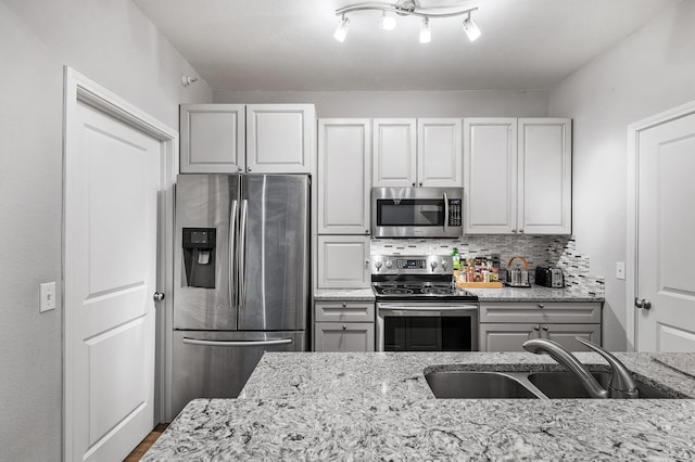 kitchen featuring light stone countertops, track lighting, tasteful backsplash, stainless steel appliances, and sink