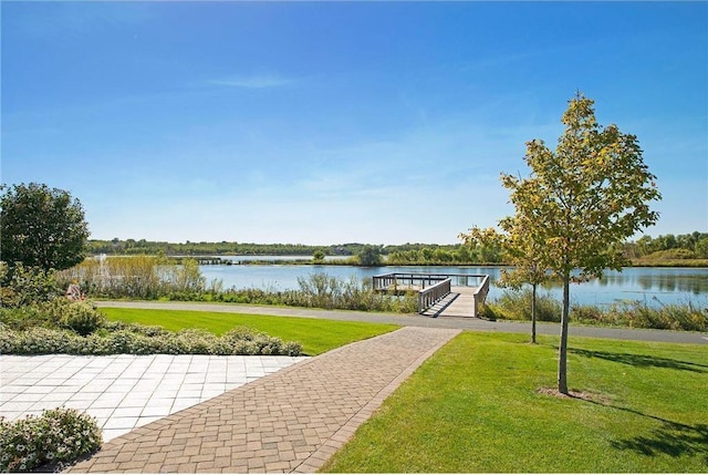 view of community with a boat dock, a water view, and a lawn