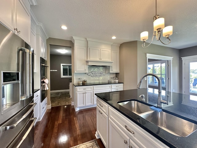 kitchen with high end fridge, hanging light fixtures, white cabinetry, and sink