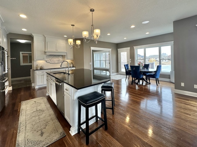 kitchen with white cabinets, dishwasher, dark countertops, a sink, and backsplash