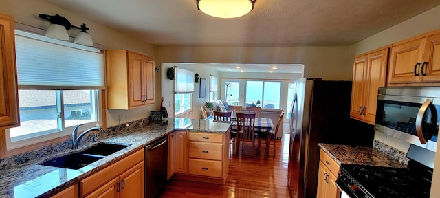 kitchen featuring kitchen peninsula, appliances with stainless steel finishes, dark stone countertops, and sink