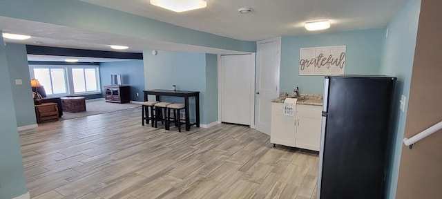 kitchen with stainless steel fridge, white cabinets, light stone counters, and light hardwood / wood-style floors