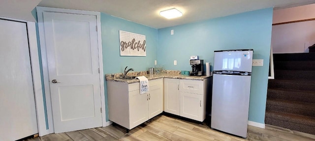 kitchen with stainless steel fridge, white cabinets, and light stone counters