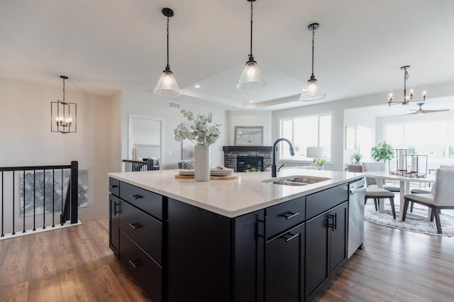 kitchen featuring a raised ceiling, a kitchen island with sink, sink, a fireplace, and hanging light fixtures