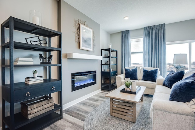 living room with a glass covered fireplace, a textured ceiling, baseboards, and wood finished floors