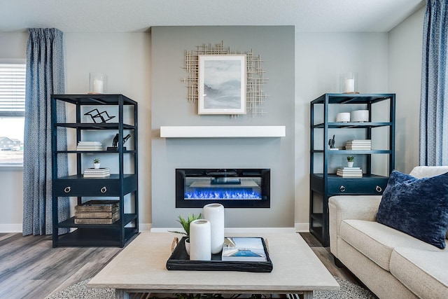 living area with a textured ceiling, wood finished floors, a glass covered fireplace, and baseboards