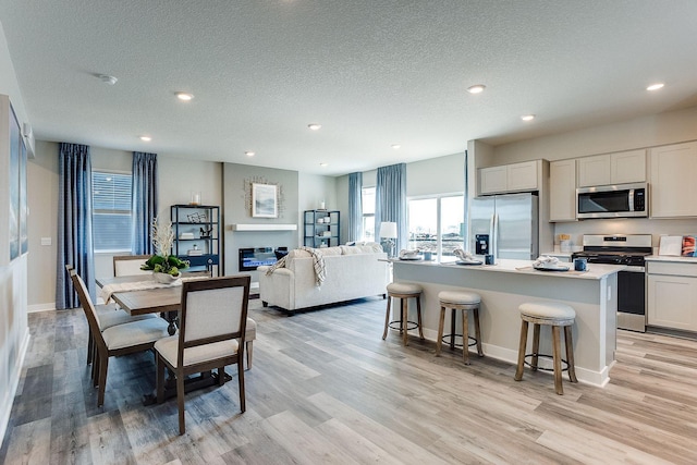 dining area with a glass covered fireplace, light wood-style flooring, a textured ceiling, and recessed lighting