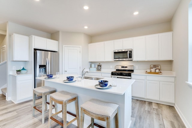 kitchen with white cabinets, stainless steel appliances, light hardwood / wood-style flooring, and a center island with sink