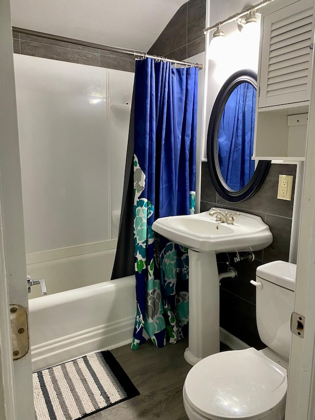 bathroom with hardwood / wood-style floors, shower / bath combination with curtain, vaulted ceiling, toilet, and tile walls