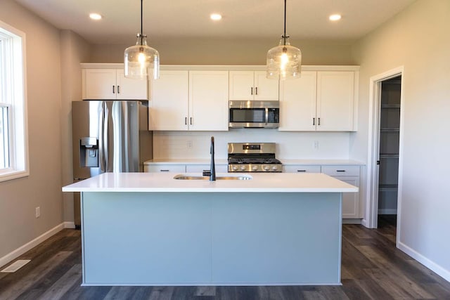 kitchen featuring white cabinetry, an island with sink, stainless steel appliances, and decorative light fixtures