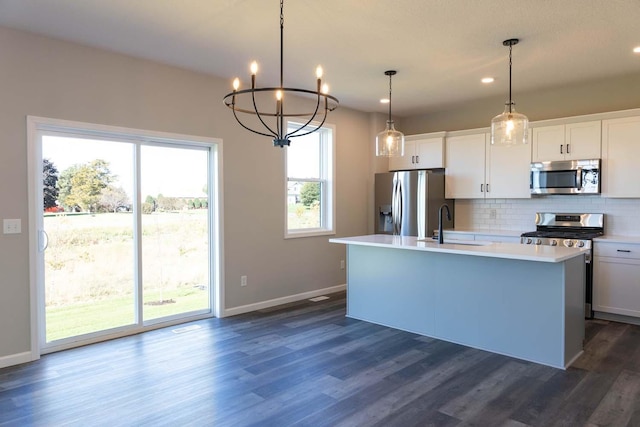 kitchen featuring white cabinetry, backsplash, decorative light fixtures, a center island with sink, and appliances with stainless steel finishes