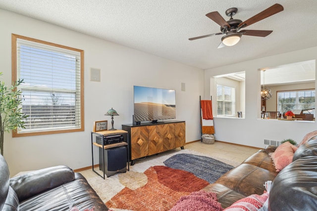 living area featuring baseboards, ceiling fan with notable chandelier, visible vents, and a textured ceiling