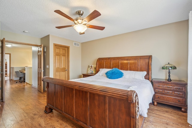 bedroom featuring light wood finished floors, visible vents, a textured ceiling, and a ceiling fan