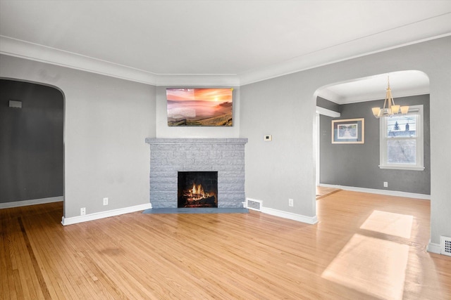 unfurnished living room featuring hardwood / wood-style floors, an inviting chandelier, ornamental molding, and a brick fireplace