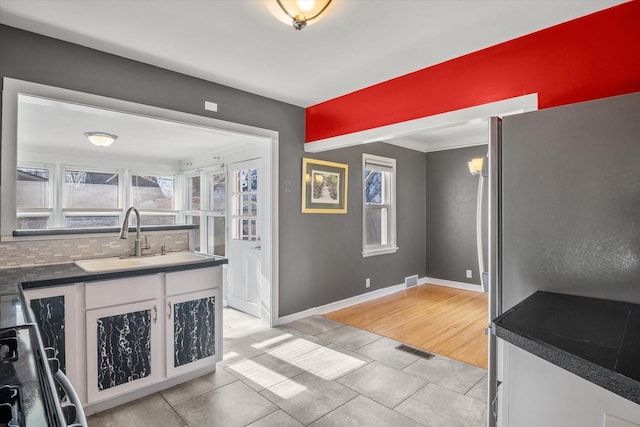 kitchen with decorative backsplash, stove, sink, white cabinetry, and light tile patterned flooring